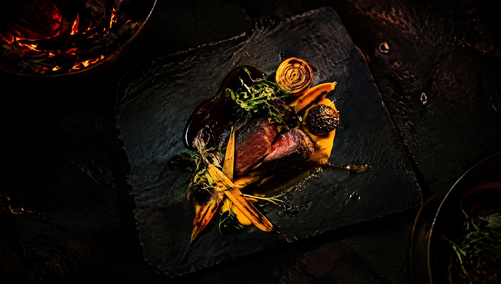 Plated dish on dark slate beside glowing embers